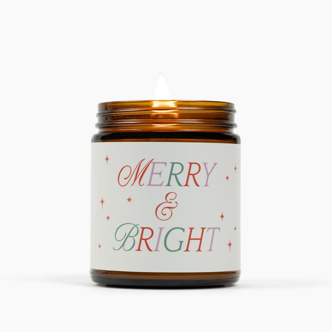 Lit amber glass jar candle with a cream colored label and festive holiday text in red green and purple: Merry & Bright.