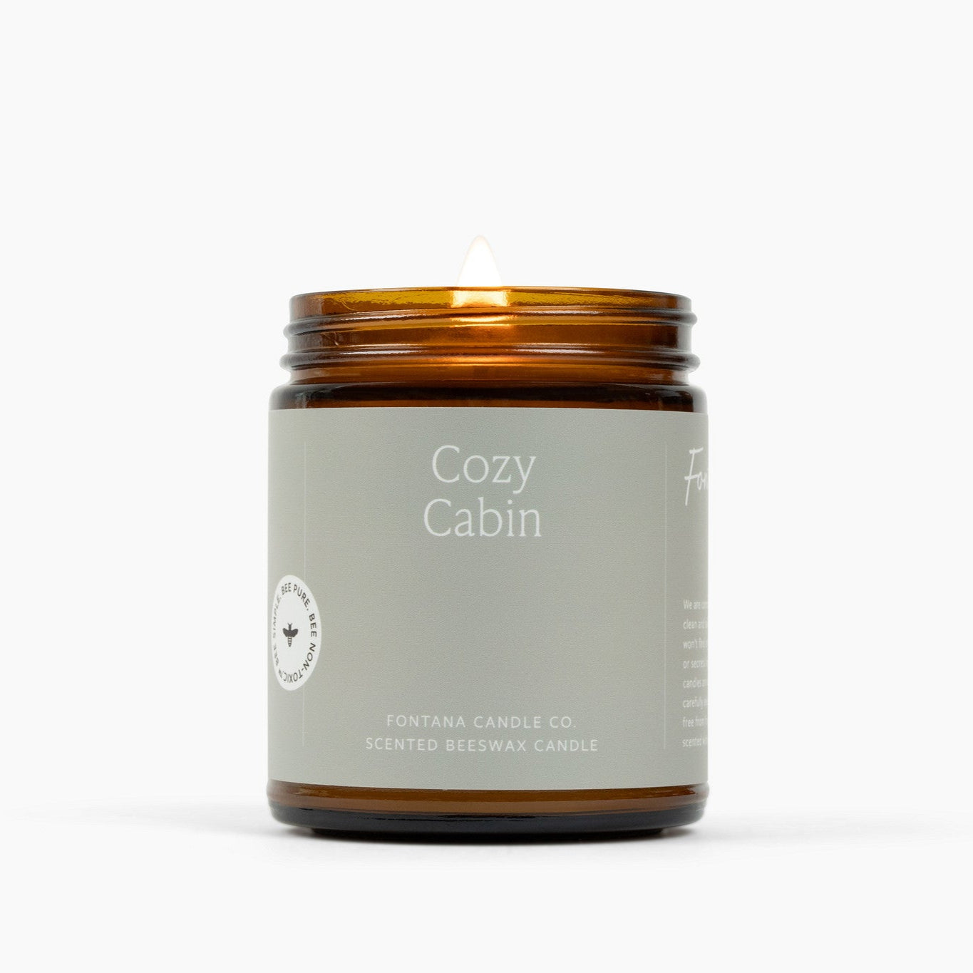 Lit amber glass jar candle with a light gray label for the scent Cozy Cabin.