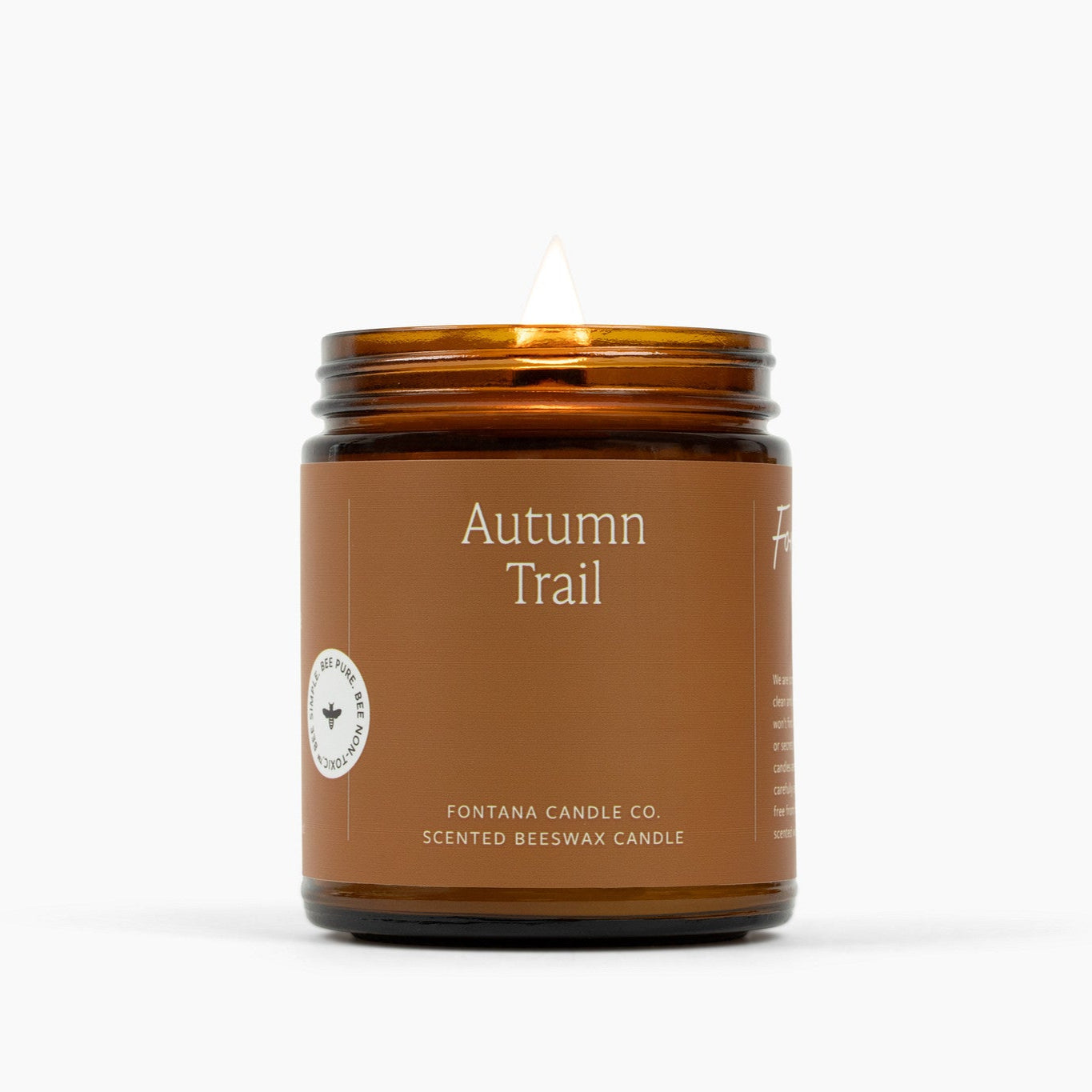 Lit amber glass jar candle with a deep brown label and the scent name Autumn Trail.