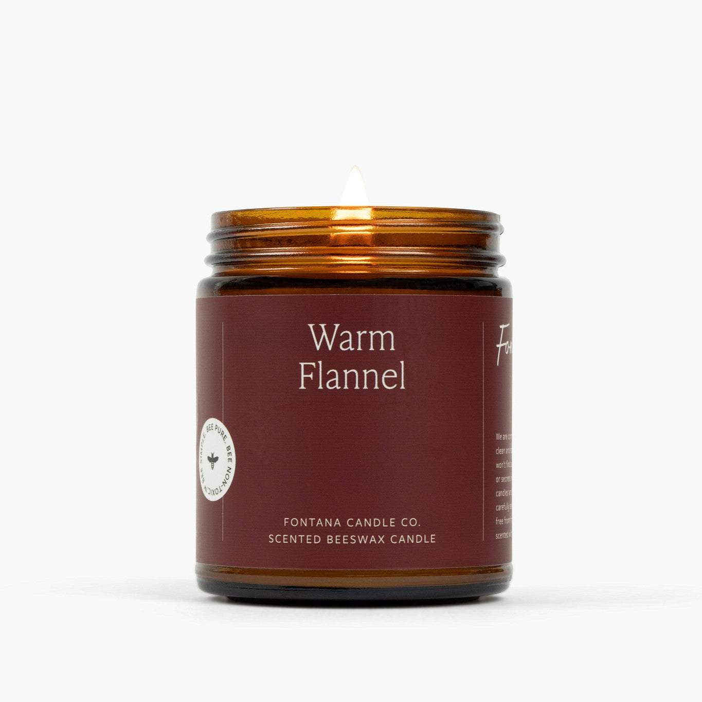 Lit amber glass jar candle with a deep red label and the scent Warm Flannel.