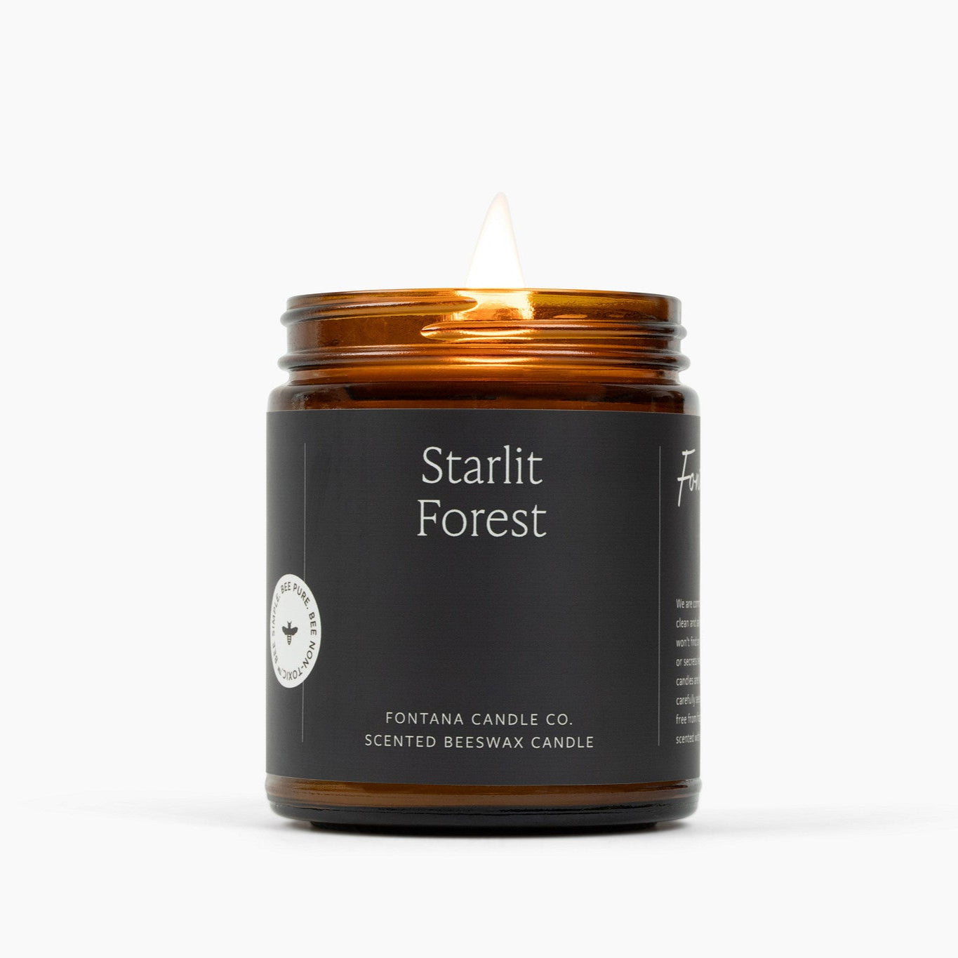Lit candle in an amber glass jar with a dark green label for the scent Starlit Forest.