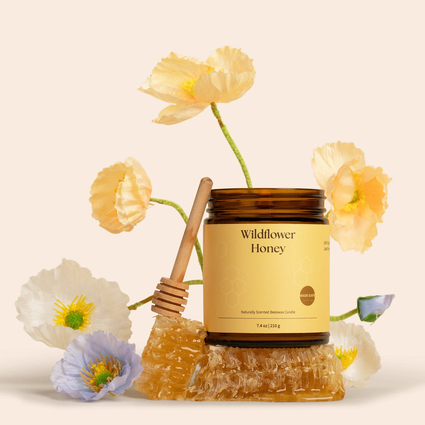 Amber glass jar candle of Wildflower Honey with honeycomb and flowers on a light background.