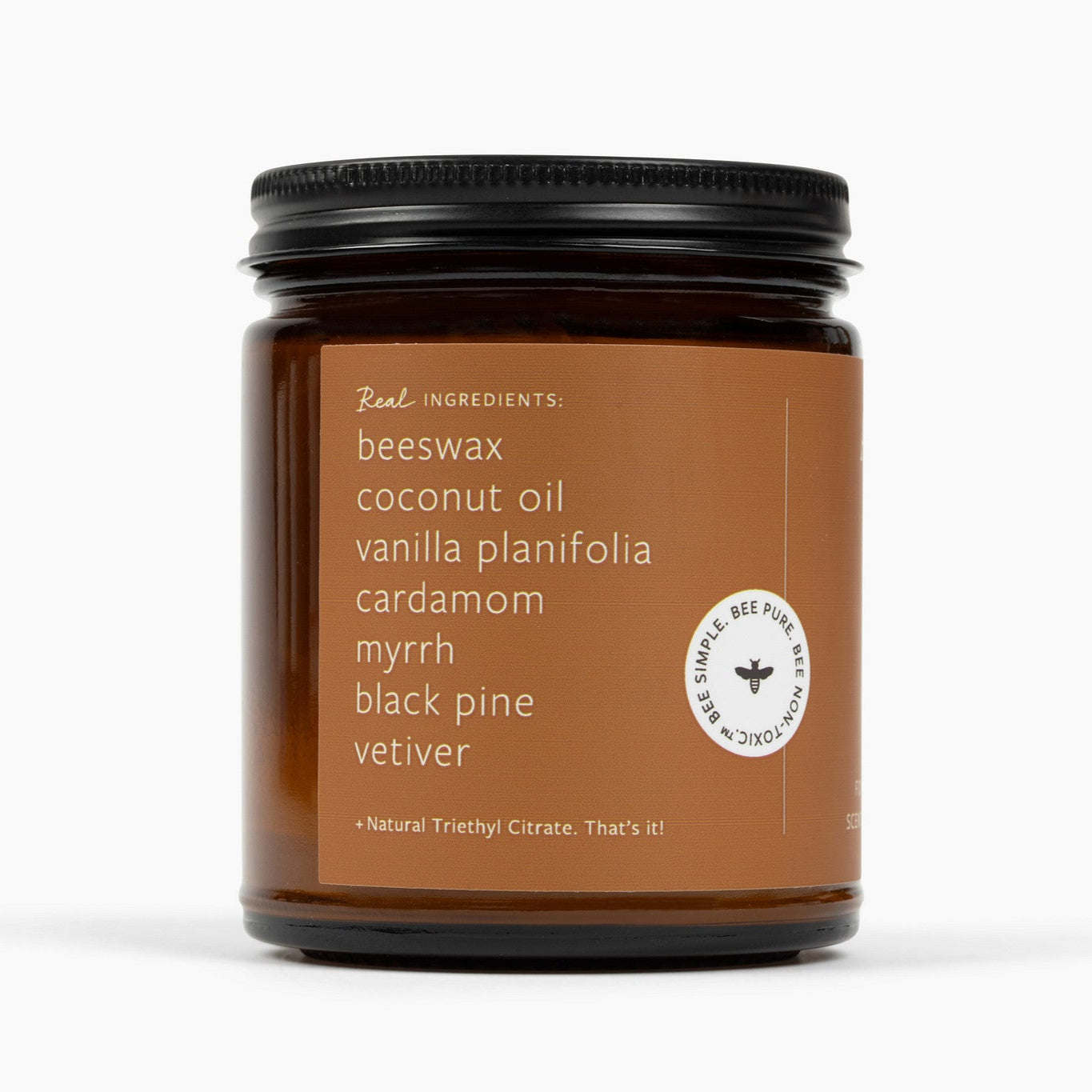 Side of an amber glass jar candle with a deep brown label and the ingredients: beeswax, coconut oil, vanilla planifolia, cardamom, myrrh, black pine, vetiver, and natural triethyl citrate.