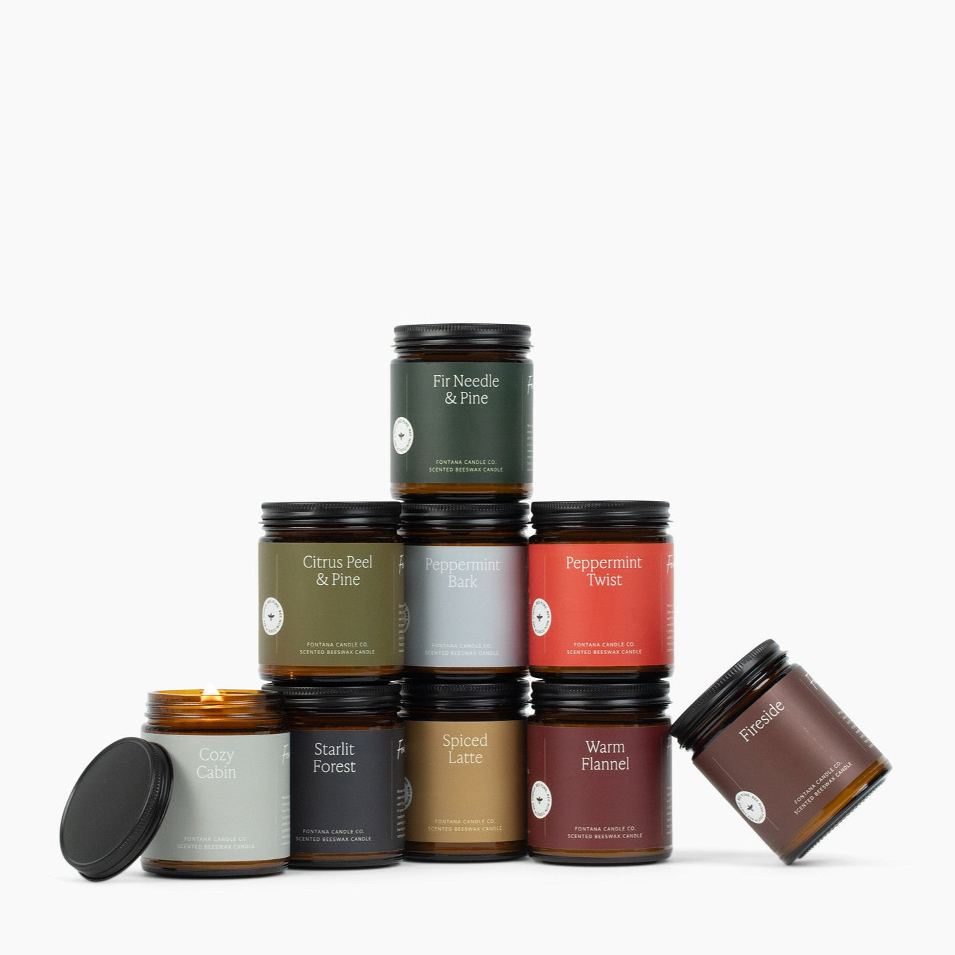 Assortment of 9 amber glass jar candles with green, red, burgundy gold, and brown labels, in front of a white background.