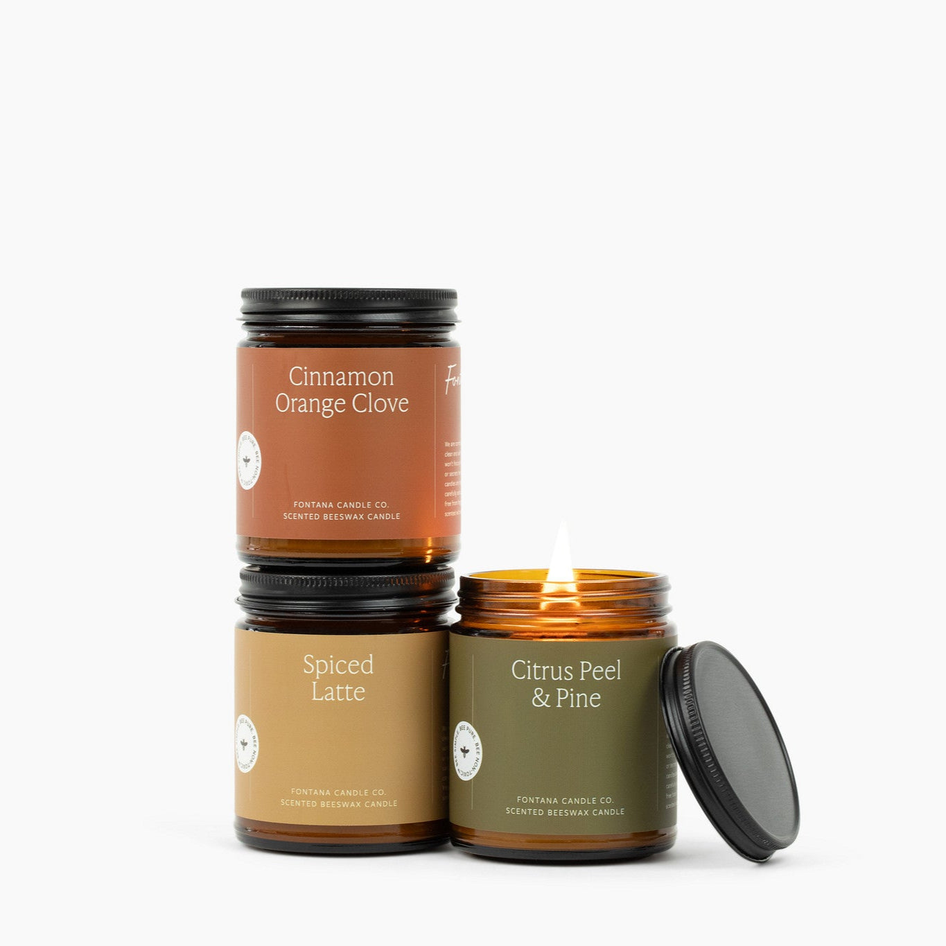 Three amber glass jar candles on a white background: Cinnamon Orange Clove, Spiced Latte, Citrus Peel & Pine.