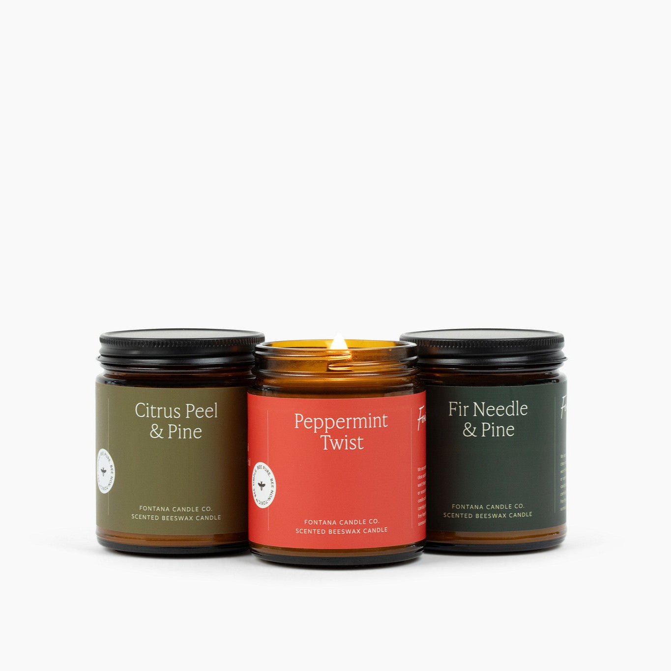 Three amber glass jar candles on a white background: Citrus Peel  Pine, Peppermint Twist, and Fir Needle and Pine.