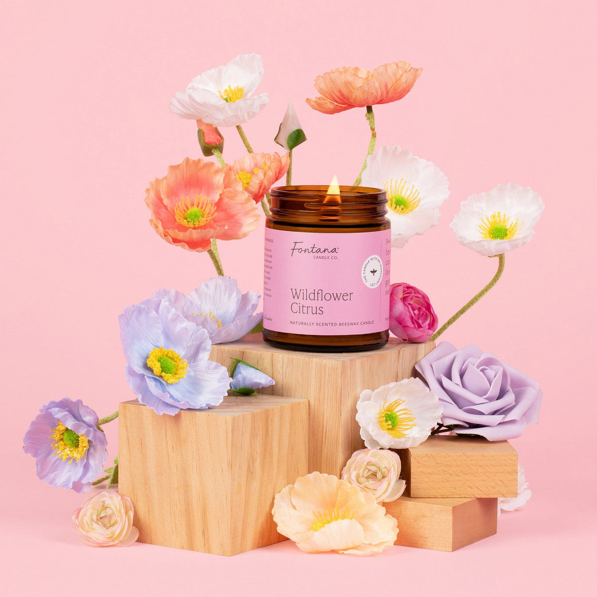a 9oz wildflower citrus jar candle posed with a variety of flowers on a pink background