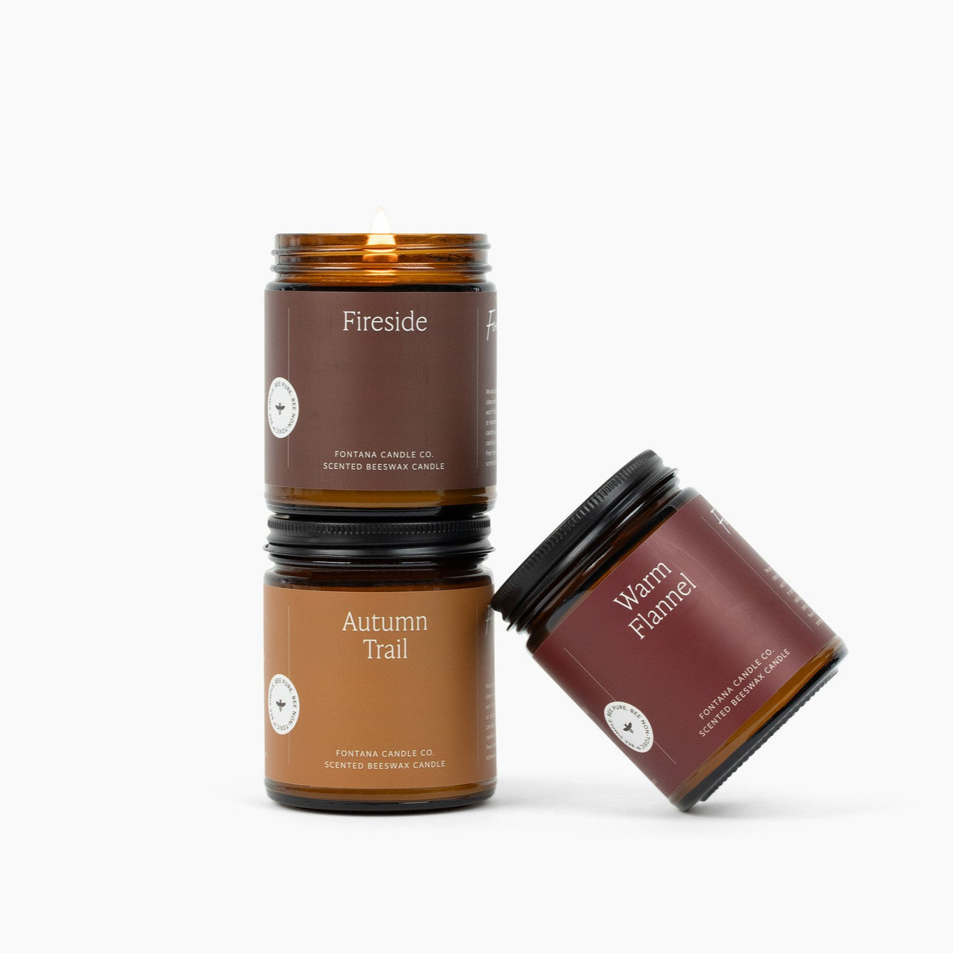 Three amber glass jar candles on a white background: Fireside, Autumn Trail, and Warm Flannel.