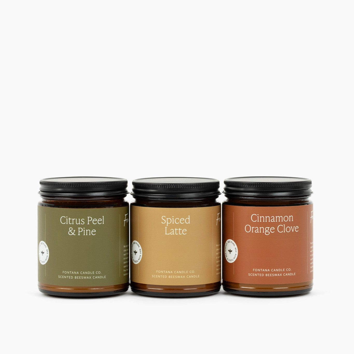 Three amber glass jar candles on a white background: Cinnamon Orange Clove, Spiced Latte, Citrus Peel & Pine.