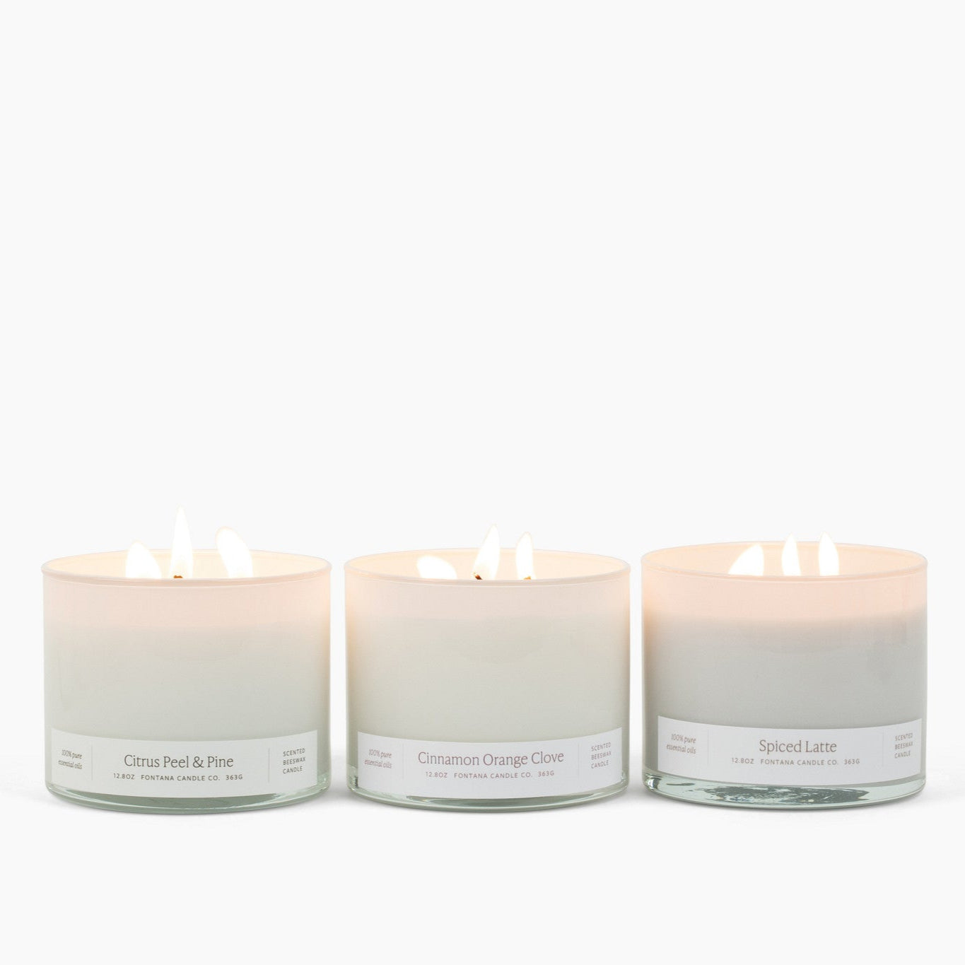 3 lit 3-wick candles in white glass vessels: Citrus Peel and Pine, Cinnamon Orange Clove, and Spiced Latte.