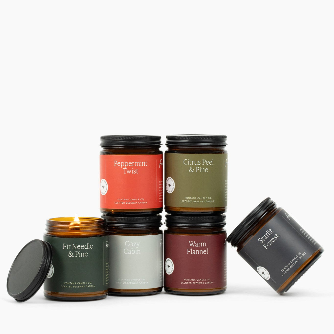 Collection of 6 amber glass jar candles with green, red, burgundy, and gray labels on a white background