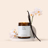 Pure Vanilla amber glass jar candle with vanilla beans and flowers on a cream background.
