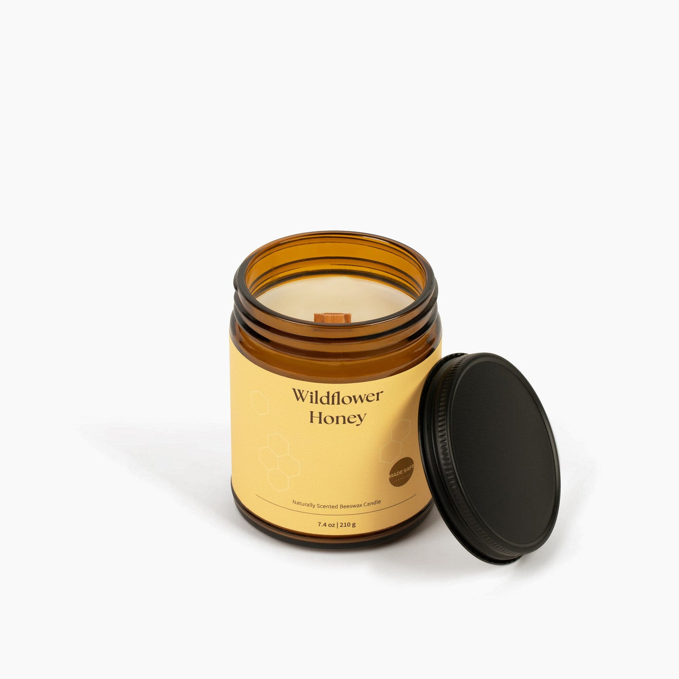 Candle in an amber jar with a wooden wick labeled 'Wildflower Honey' on a white background
