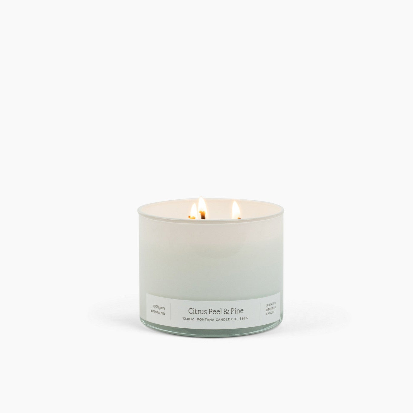 Lit 3 wick candle burning in a white glass container with a Citrus Peel and Pine scent label. 