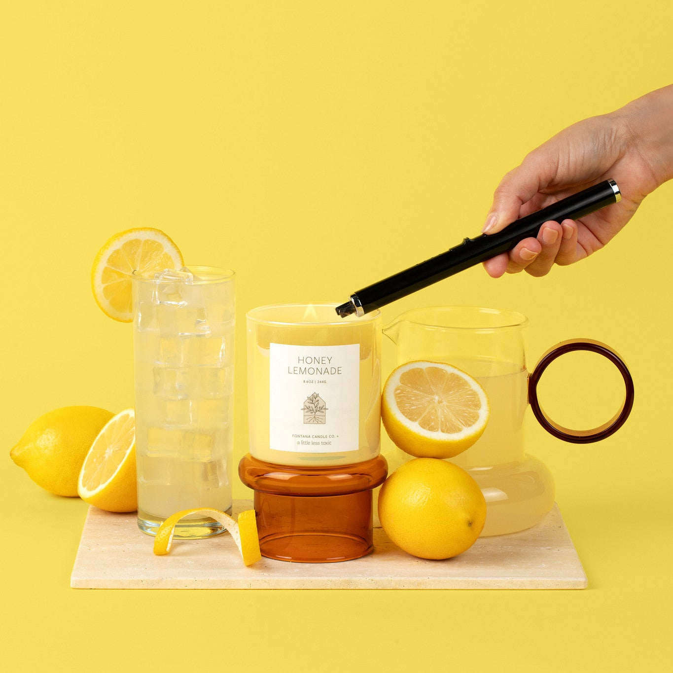 Yellow glass candle on front of a yellow background with lemonade and lemons.