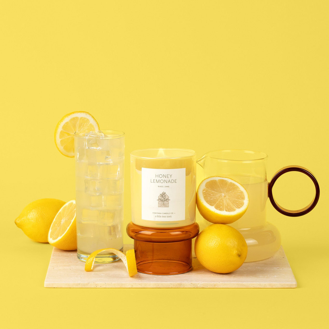 Yellow glass candle with lemon slices and a glass of lemonade on a yellow background.