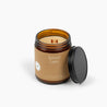 Unlit amber glass jar candle with a brown label and wooden wick. 
