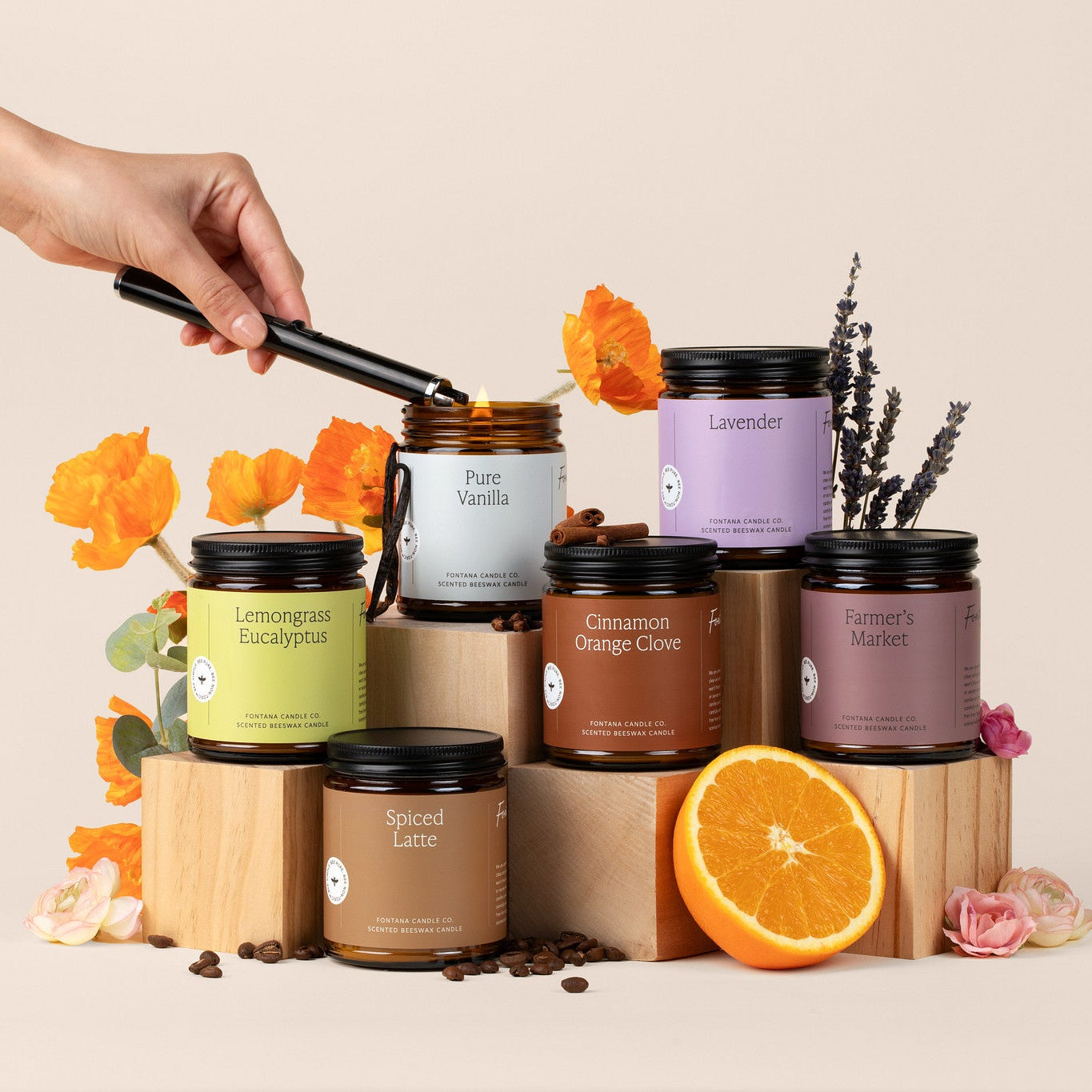 6 amber glass jar candles on a beige background, surrounded by flowers, spices, and oranges.