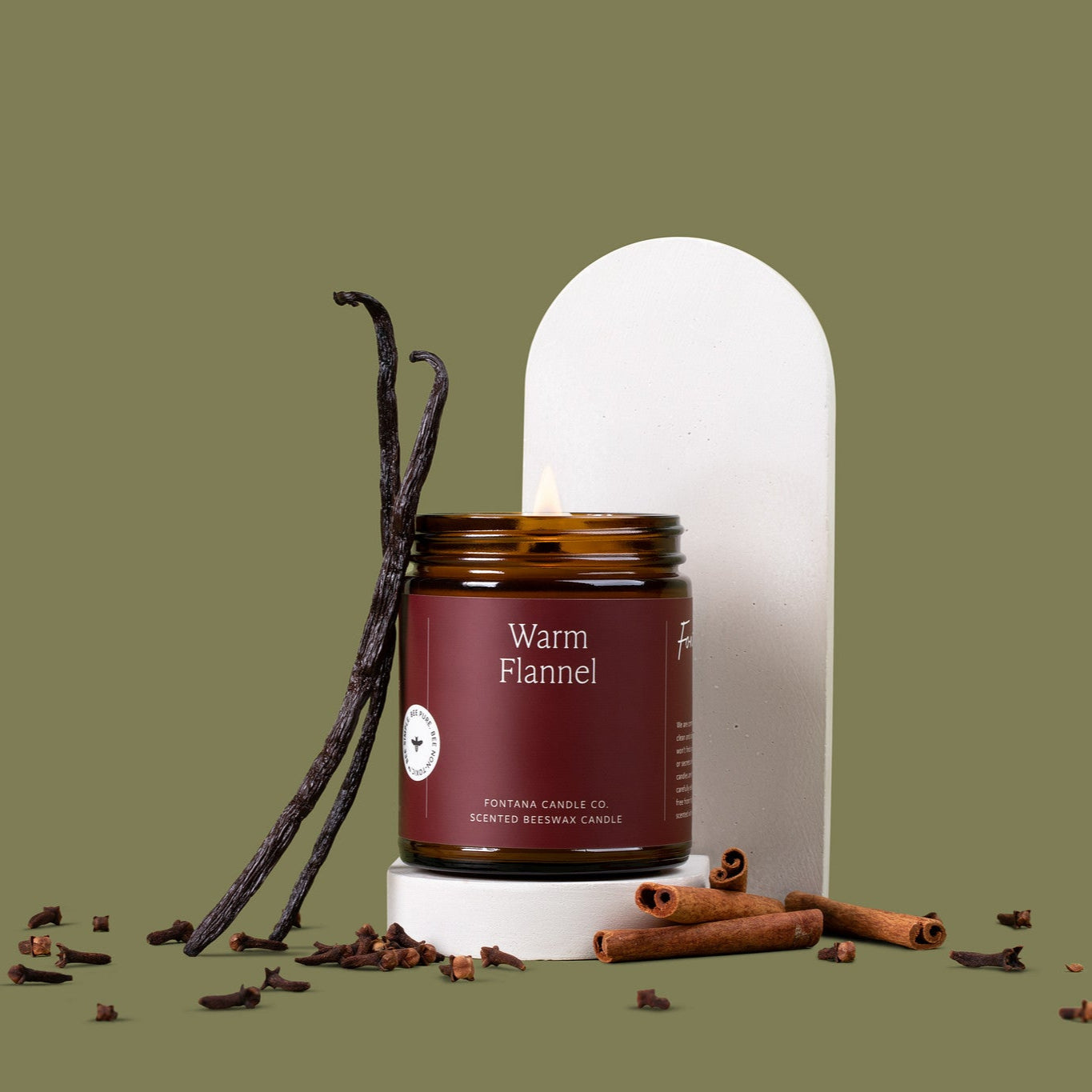 Amber glass jar candle labeled 'Warm Flannel' with vanilla beans and cinnamon sticks on a green background