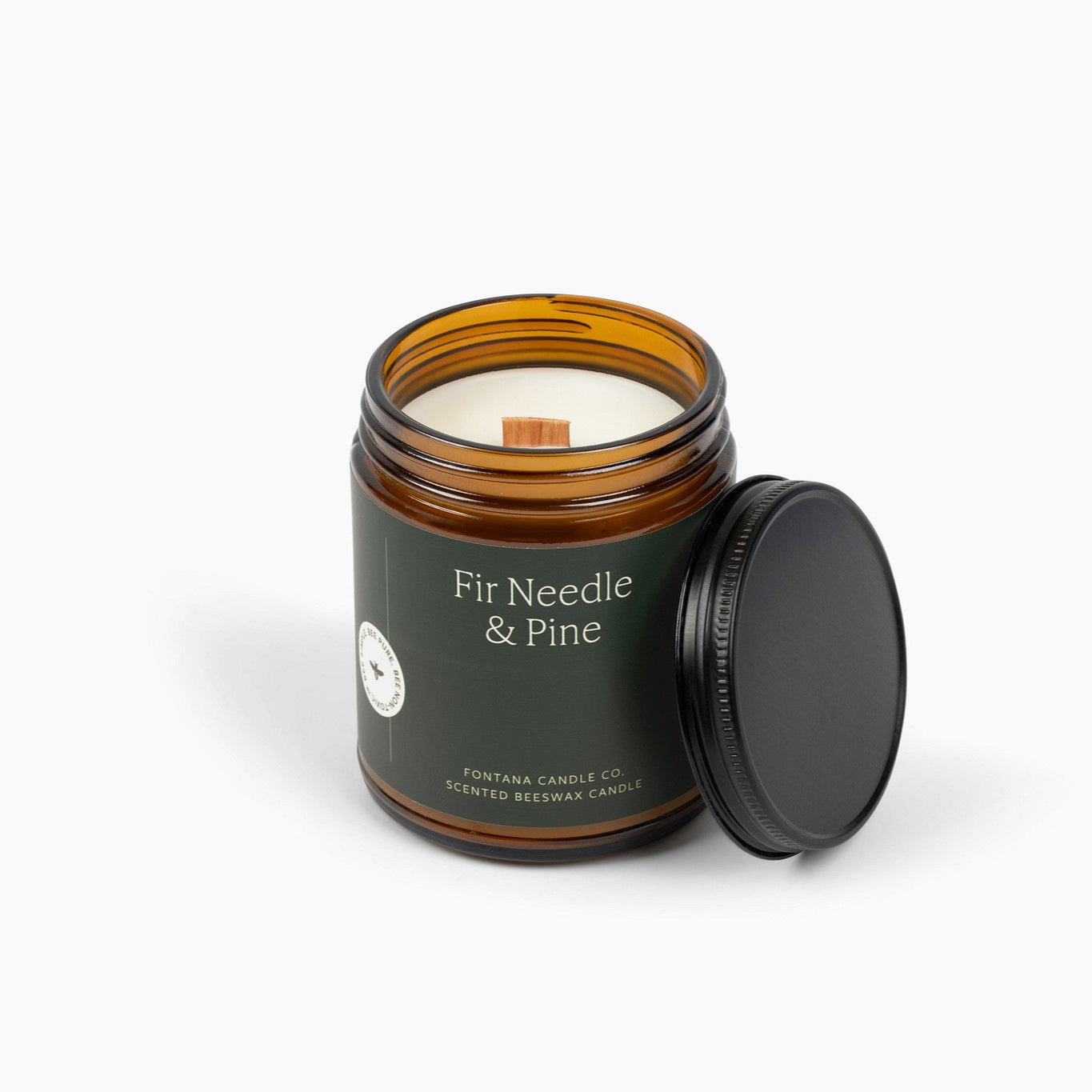 Unlit amber glass jar candle with a dark green label and wooden wick.