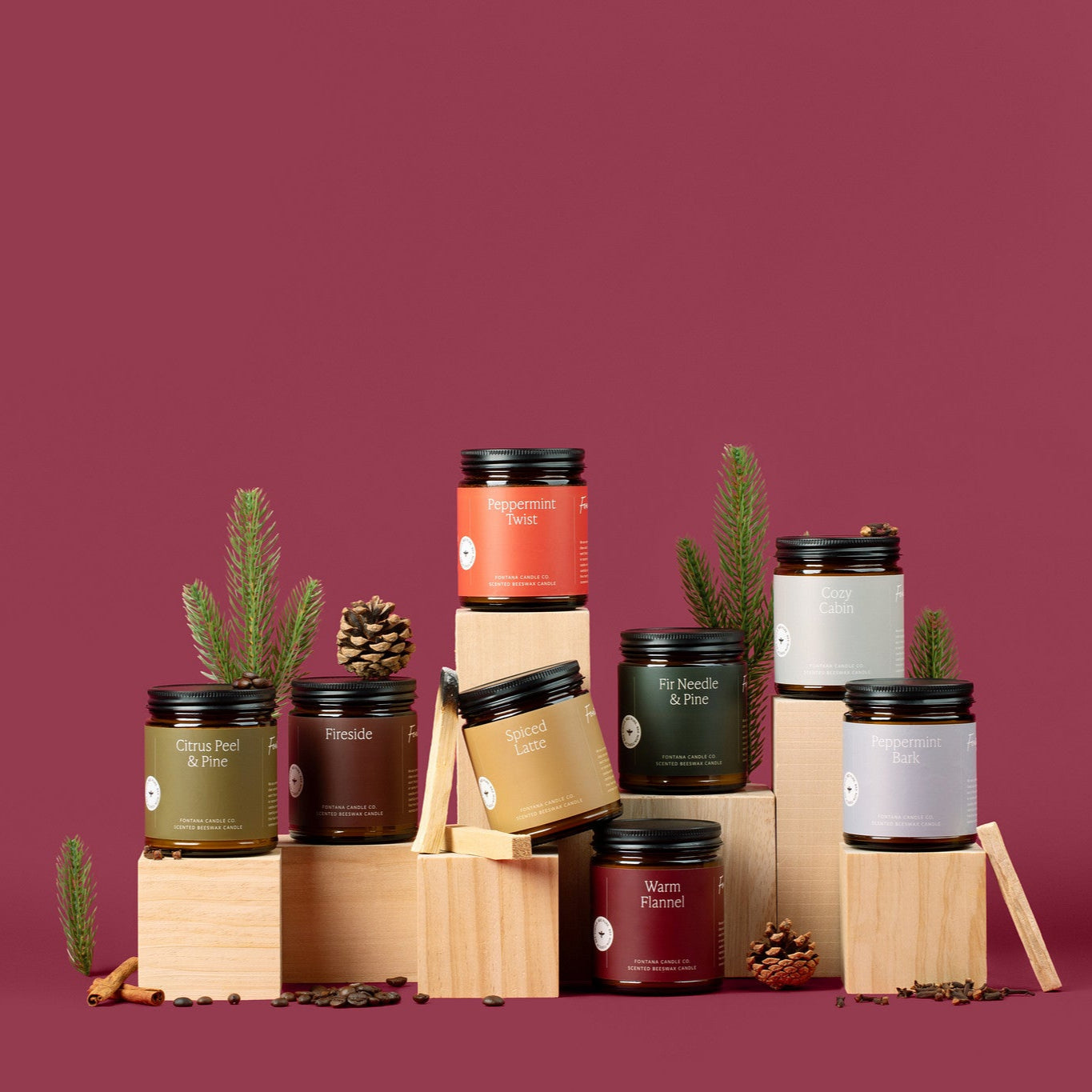 Collection of holiday amber glass jar candles and pinecones, spices, and pine branches. on a red background