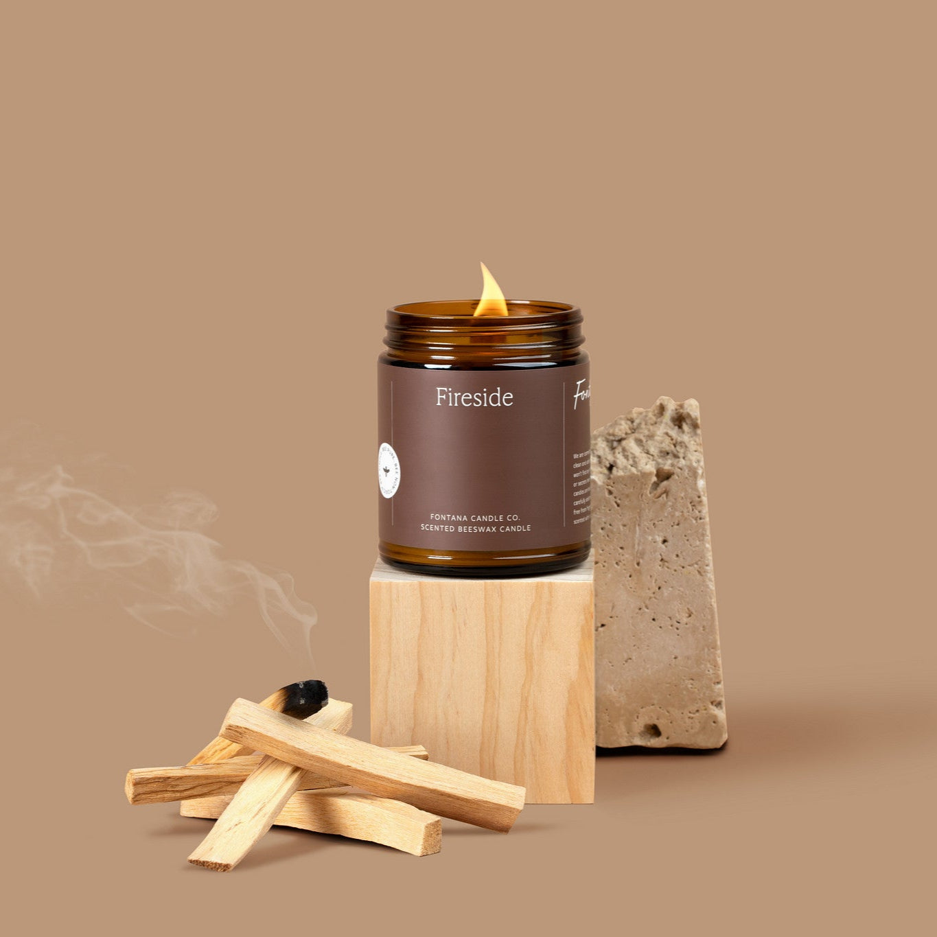 Amber glass jar candle labeled 'Fireside' with lit Palo Santo sticks on a beige background