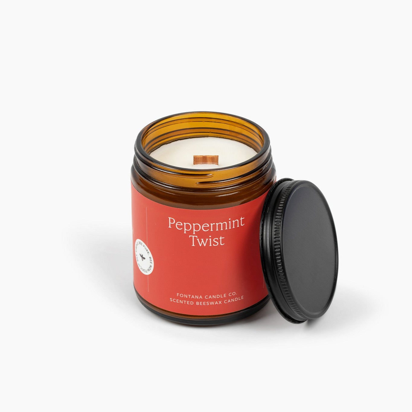 Unlit amber glass jar candle with a red label and wooden wick. 