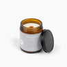 Unlit amber glass jar candle with a wooden wick and a light gray label with the scent Peppermint Bark.