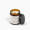 Unlit amber glass jar candle with a wooden wick and a cream colored label with the festive holiday text that says: Merry & Bright.
