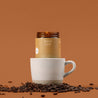 Spiced Latte coffee amber glass jar candle with a white mug and scattered coffee beans on a brown background.
