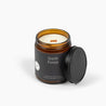 Unlit amber glass jar candle with a dark green label for the scent Starlit Forest and a wooden wick.