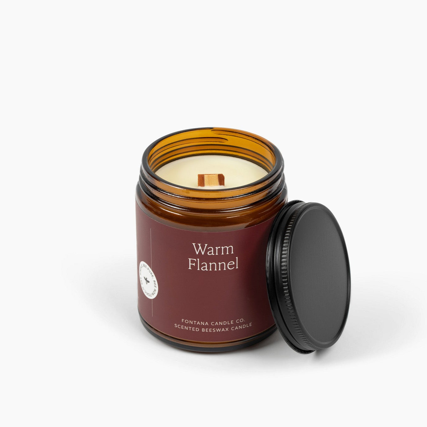 Unlit amber glass jar candle with a deep red label and a wooden wick.