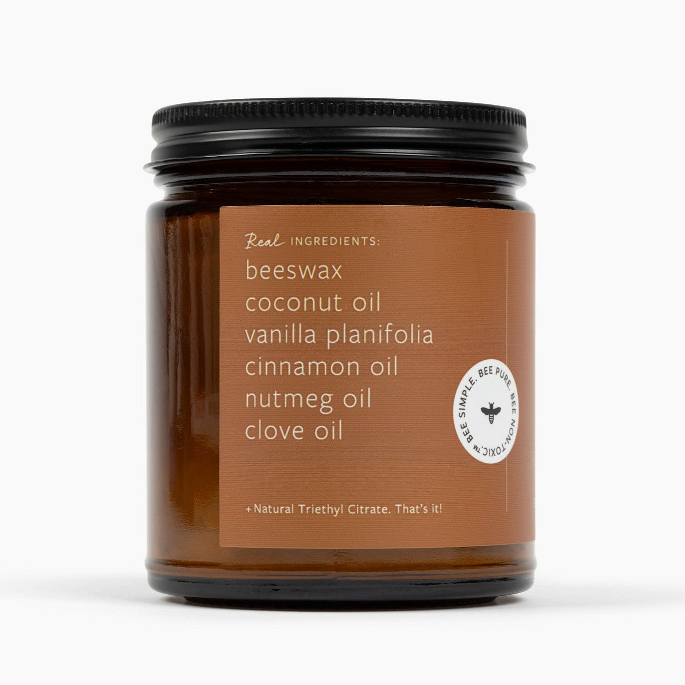 Side view of amber glass jar candle with a brown label and ingredients: beeswax, coconut oil, vanilla planifolia, cinnamon oil, nutmeg oil, and clove oil.